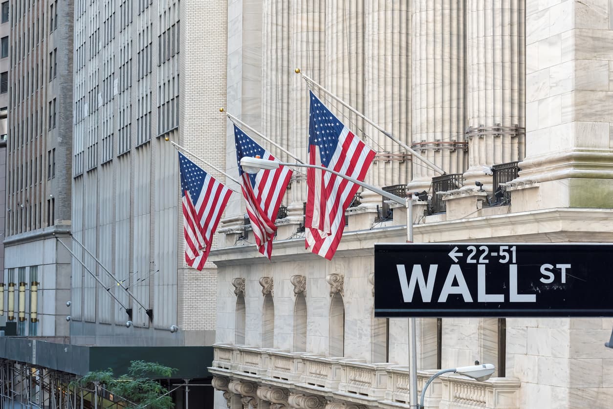 Wall Street sign with US flags hanging from a financial district building, representing the US brokerage industry behind US brokerage account closures for Americans abroad