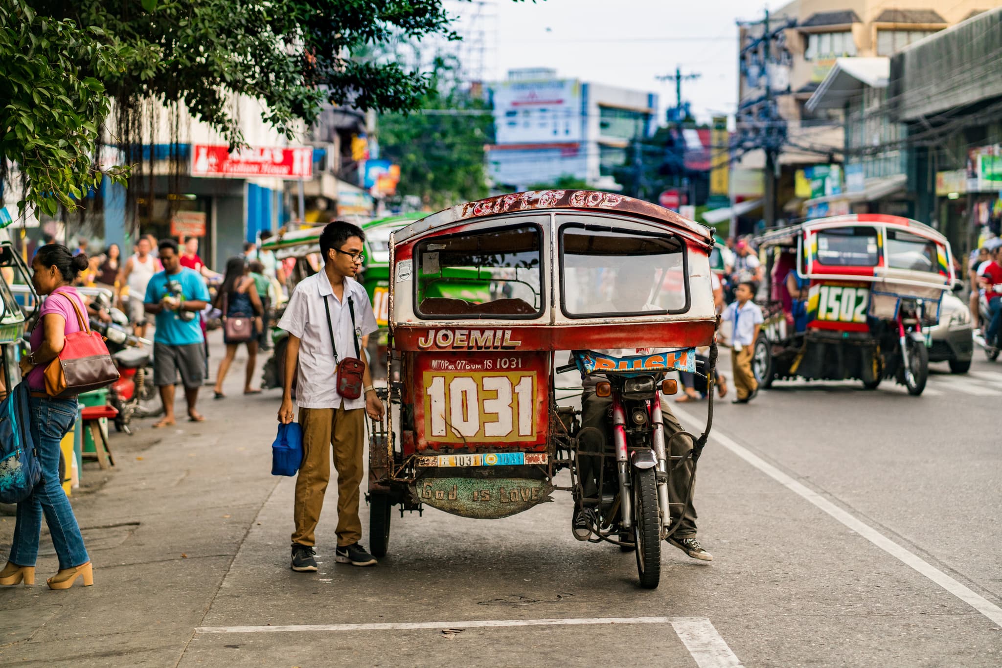 Red motorized tricycle on a busy street in the Dumaguete area, with pedestrians and other tricycles nearby.