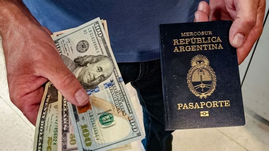 Person holding U.S. $100 bills in one hand and an Argentine Mercosur passport in the other, illustrating the cost of Argentina citizenship by investment