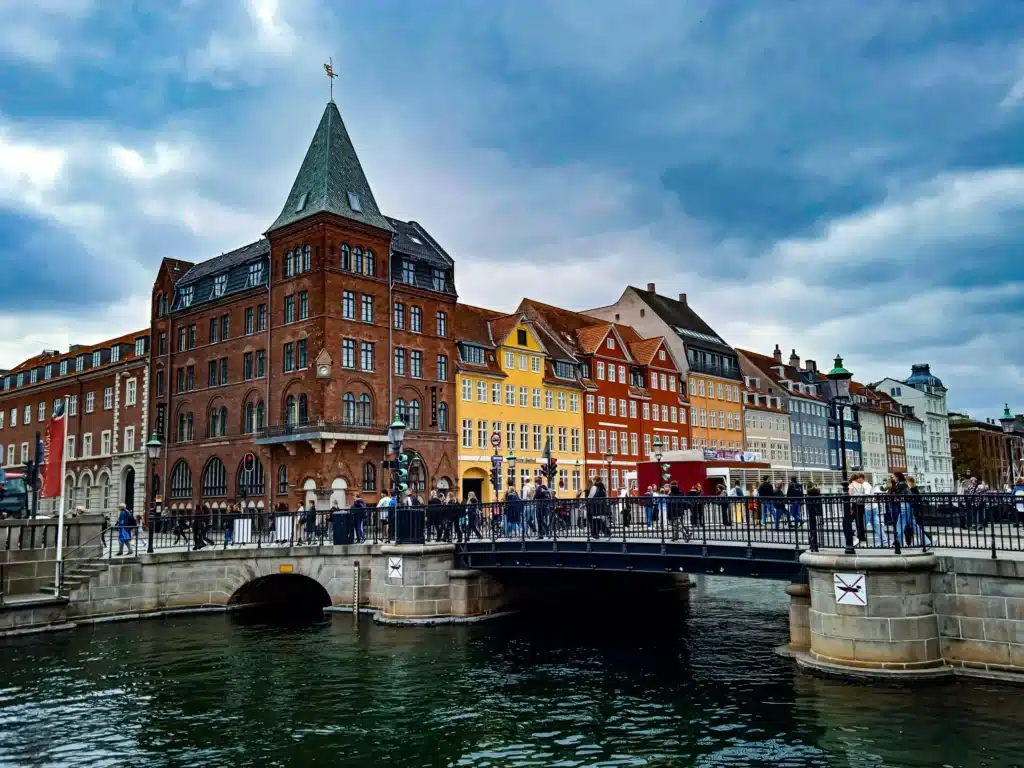 Transgender Healthcare in Europe: The Best Places for Gender-Affirming Care 4 A view of the **Nyhavn** canal in Copenhagen, Denmark, on a cloudy day. The canal is lined with colorful, historic buildings, with a metal bridge crossing the water in the foreground.