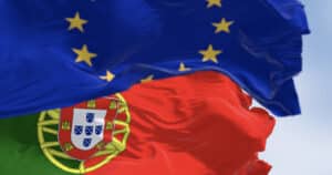 American Emigration Revue 10 Close-up of Portugal and the European Union flags waving on a clear day. Symbolizing Portugal's place among the top European digital nomad visas.