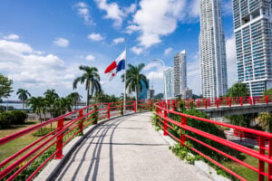 Panama City, Panama - A modern urban landscape featuring high-rise residential towers and a distinctive red pedestrian bridge in the foreground. The scene highlights contemporary architecture, urban development, and vibrant city infrastructure under a bright sky. Symbolizing one of the reasons wealthy Americans retiring in Panama is a growing trend.