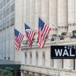 Wall Street sign with US flags hanging from a financial district building, representing the US brokerage industry behind US brokerage account closures for Americans abroad