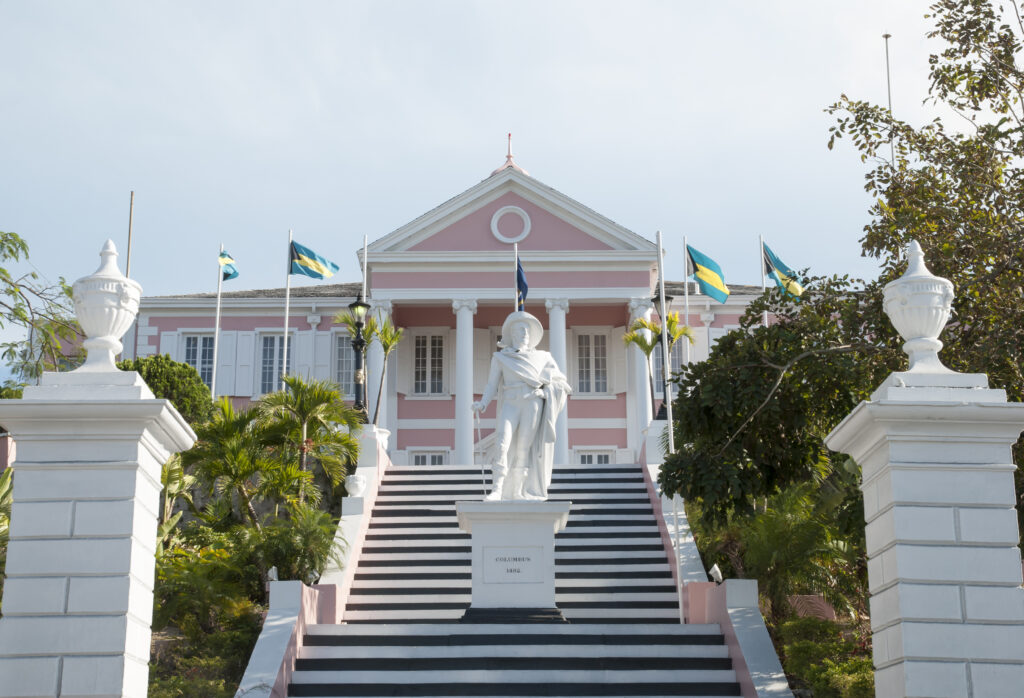 Government House in Nassau with Bahamian flags and the Columbus statue, the seat of government weighing the Bahamas permanent residency amendment