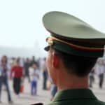 Uniformed Chinese officer watching a crowd in Beijing, where American seismologist Youlin Chen has been detained in China since 2024.