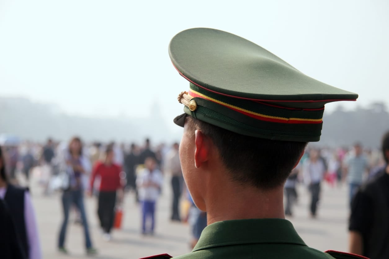Uniformed Chinese officer watching a crowd in Beijing, where American seismologist Youlin Chen has been detained in China since 2024.